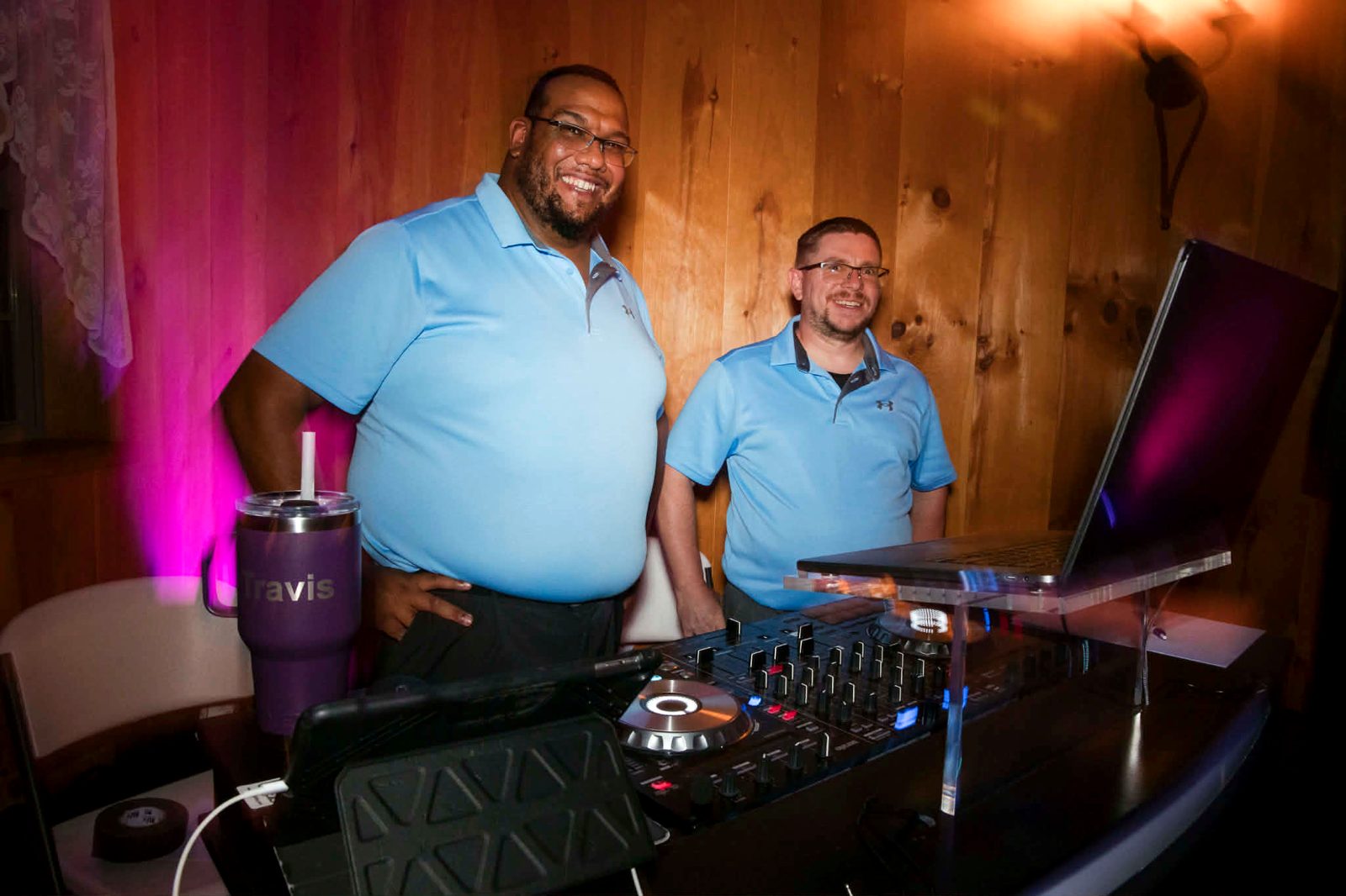 Travis and a fellow DJ smiling behind the decks under pink uplighting